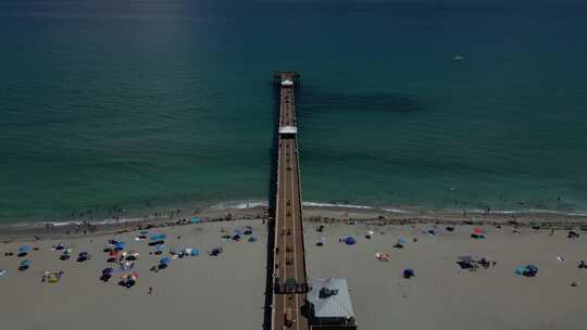 空中无人机镜头，多莉镜头和海滩上有人的长延伸码头。对称