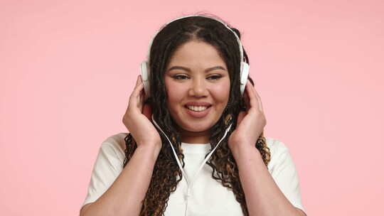 女人在粉色背景前用耳机听音乐感到快乐