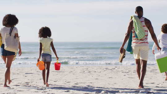 非裔美国父母和他们的孩子在海滩上拿着海滩设备