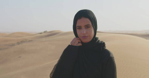 穆斯林女人在多风的沙漠中看着相机