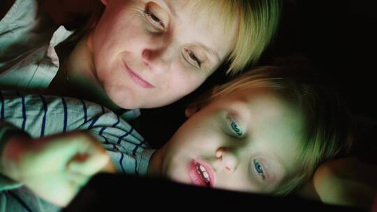 黑夜妈妈和女儿躺在床上玩平板电脑视频素材模板下载