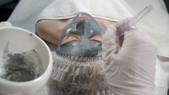 年轻女子躺在水疗美容院，脸上戴着深色面具。美容