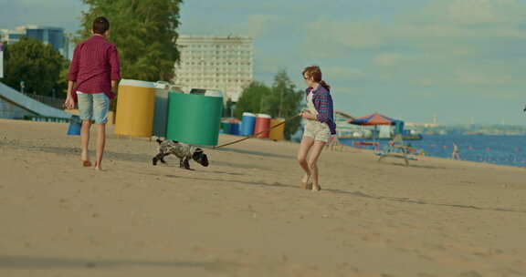 有趣的女孩用皮带拴着一只小狗，他们跑过沙滩