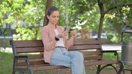 年轻女子在公园用信用卡和电话在线购物