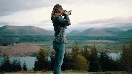 女人站在岩石上给下面的山谷拍照