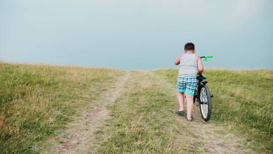 小男孩推着自行车走在田野小路上