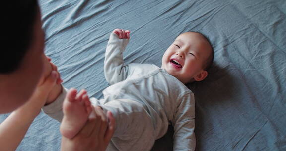 可爱的小婴儿躺在床上被妈妈逗开心大笑