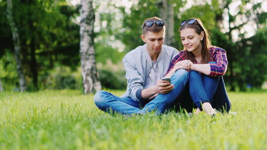 情侣坐在草地上看手机