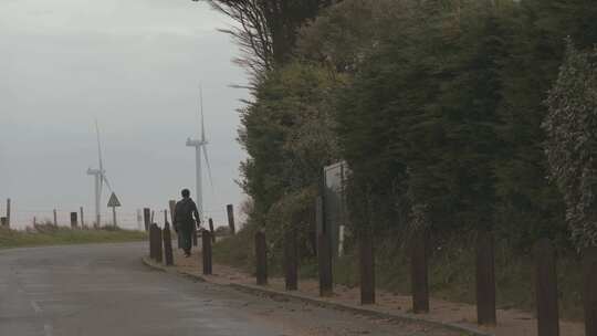 一名男子在靠近道路的人行道上走向风力涡轮