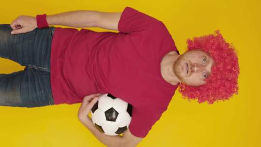 身穿红色制服的足球迷在黄色背景下欢呼的垂直镜头视频素材模板下载