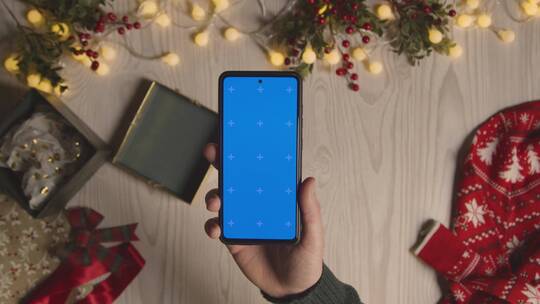 在圣诞装饰物上方拿蓝屏手机的手
