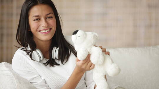 快乐的女孩坐在沙发上玩泰迪熊玩偶