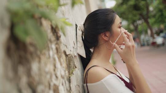 有吸引力的亚洲女人戴着白色防护口罩，侧视靠墙，新冠病毒，环境保护，白天，新常态，户外场景，亚洲女士戴上口罩