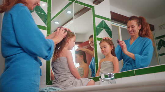 快乐的妈妈洗澡后在镜子前梳理她可爱的小女