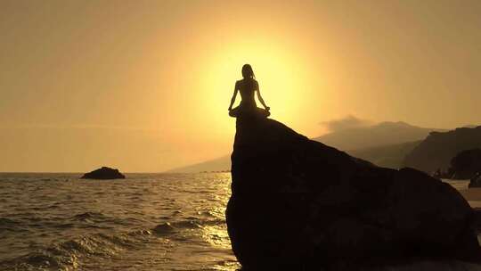 夕阳下女孩在海边岩石上打坐冥想视频素材模板下载