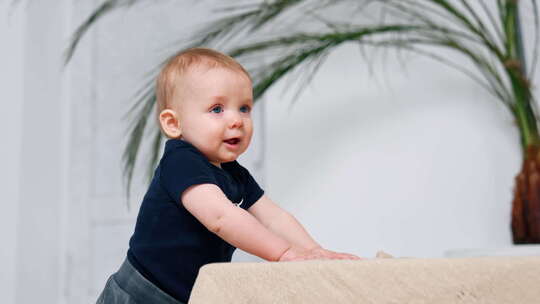 可爱的红头发男婴抱着沙发站着。可爱的小婴