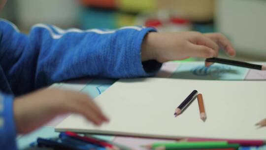 孩子拿着彩色铅笔在白纸上画画