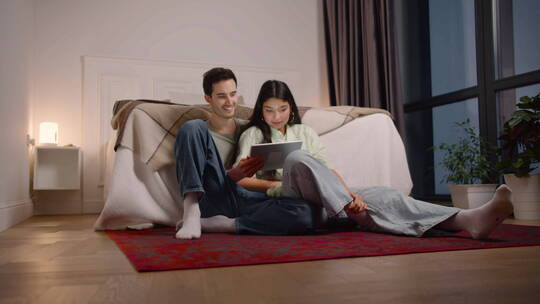 一对夫妇坐在家里的地板上看平板电脑