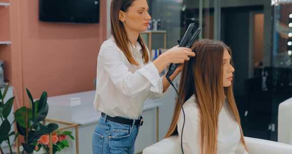 专业理发师造型师在美容工作室为美丽的女人拉直头发