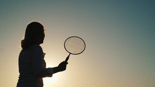 年轻女子在日落时打羽毛球的剪影