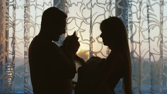 女人抱婴儿男人抱狗站在窗前的剪影