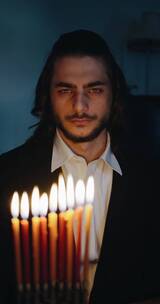 一个男人坐在光明节燃烧的蜡烛后面竖屏