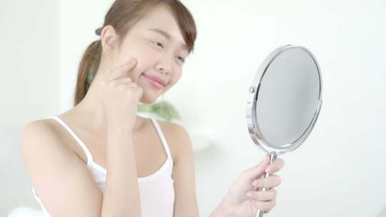 美丽的年轻亚洲女人微笑着看着健康检查皮肤护理高加索人的镜子。