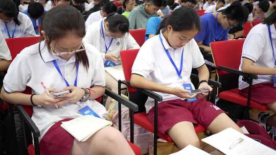 学生们坐在礼堂内使用手机的场景