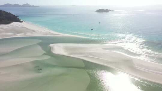 旋转的太阳光线掠过浅滩泻湖，远处有帆船