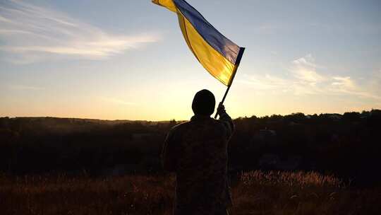 身穿军装的年轻人在日落背景下挥舞乌克兰国