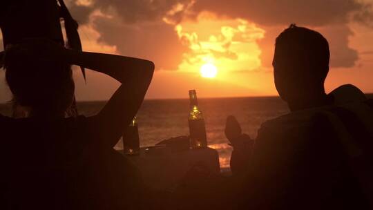 日落时分情侣在海滩上喝啤酒