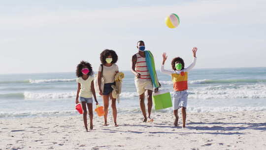 非洲裔美国父母和他们的孩子戴着口罩，在海滩上携带海滩设备
