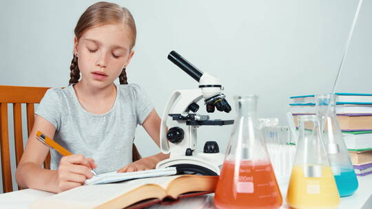 女孩在显微镜旁写东西视频素材模板下载