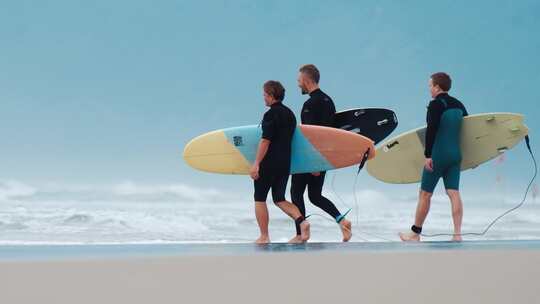 三个冲浪者带着冲浪板走在海滩上，进入海洋