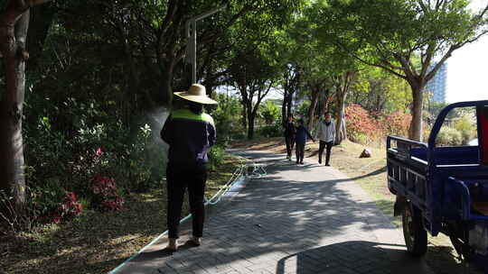 公园内工人用水管给绿植浇水