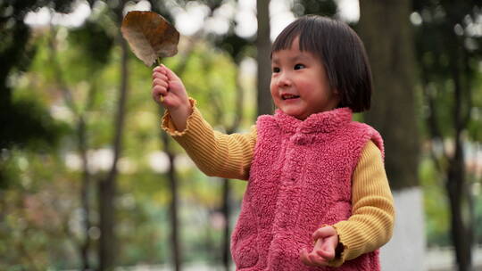 小女孩在秋天的公园里拿着一片树叶玩耍