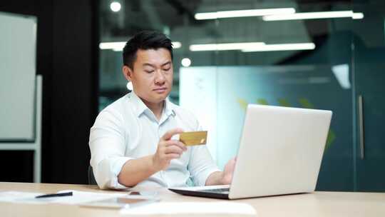 亚洲商人在办公室的笔记本电脑上进行在线支
