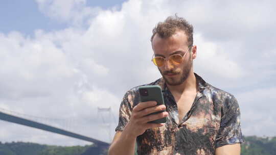 年轻体贴的男人在海边通过电话发短信。视频素材模板下载