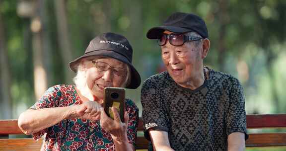 老年夫妇在公园长椅上看手机聊天