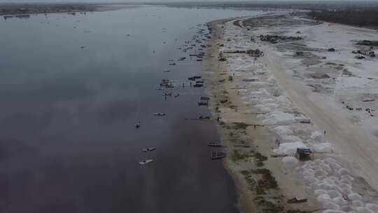 一架无人驾驶飞机沿着达喀尔粉色湖岸移动，显示了盐堆和船视频素材模板下载