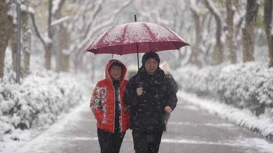 雪地里夫妻打伞有说有笑的走路