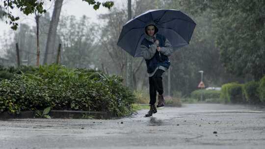 拿着雨伞的男孩在雨中跳上跳下