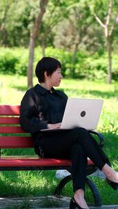 坐在公园长椅上使用笔记本电脑办公的美女