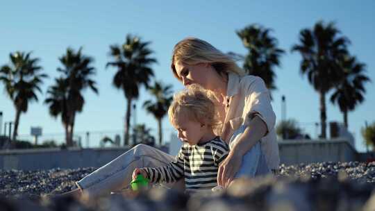 棕榈树背景下，美丽的女人和她的小儿子在鹅卵石海滩上