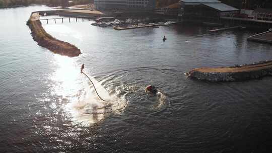 男性杂技演员白天在水上飞板上表演技巧，水上滑板车漂浮在附近