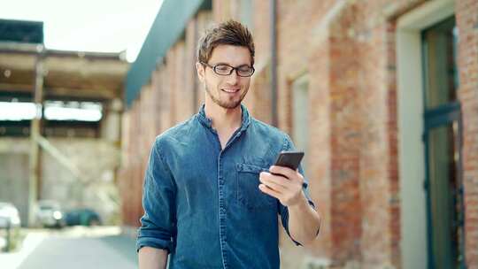 年轻英俊的男人用智能手机走在城市街道上。