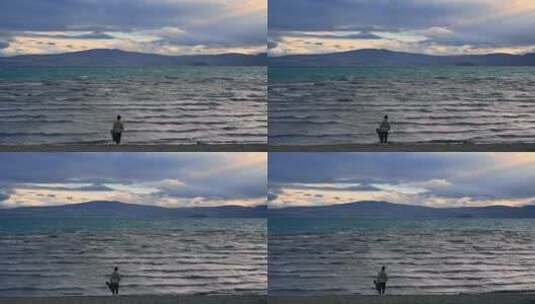男人提着吉他箱站在黄昏的西藏拉昂错湖边高清在线视频素材下载