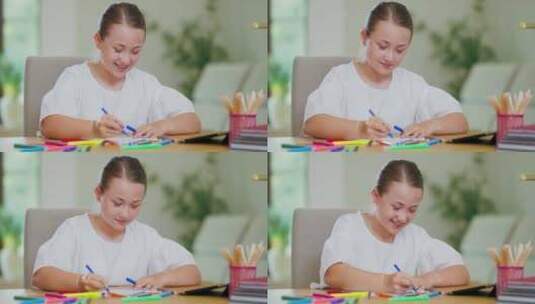 特写镜头专注于微笑的青少年女孩在书桌上用蓝色毛毡笔在白纸笔上画画高清在线视频素材下载