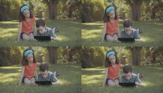 姐姐和弟弟趴在草地上玩电脑高清在线视频素材下载