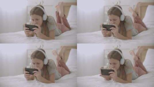 女人戴着耳麦趴在床上玩手机高清在线视频素材下载